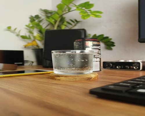 Clean drinking glass filled with fresh water sitting on a bright wooden office desk